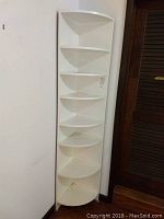 Tall white corner shelf unit positioned in a corner, showing full height and multiple shelves.