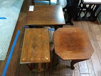Three wooden side tables grouped together on wooden floor, one octagonal table visible with wear and scratches.