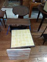 Three wooden side tables including square one with beige tiles on top, other two with dark wood and signs of wear