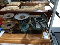 Photo shows six vintage metal incense burners displayed on a glass table with a sofa in the background.