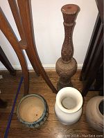 Photo showing three ceramic pots and one carved wooden plant stand on floor.