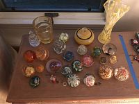 Wide shot showing entire collection of glass paperweights and glassware items on wooden table.