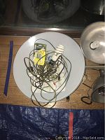 Overhead oval light with reflection, showing metallic surface and cords attached, surrounded by stands and other lighting equipment