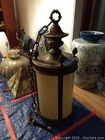 Full view of the vintage hanging lamp showing cylindrical opaque glass body with metal framing and heavy chain.