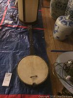 Full view of antique 4-string banjo laid flat on a blue tarp showing wooden neck, circular drum body with skin head, strings in place.
