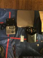 Photo showing vintage typewriter with protective cover, small Grundig emergency radio, and Tasco binoculars in leather case on tarp.