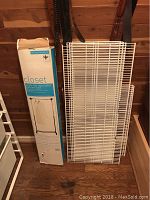 Boxed Elfa clothes rack closet frame and extra white wire shelving panels, standing upright on wooden floor.