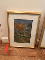 Framed painting of autumnal trees with buildings in the background in a gold frame