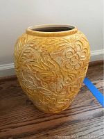 Front view of the yellow pottery vase showing carved floral and bird designs.