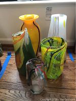 All five assorted glass vases grouped on a wooden floor showing various colors and shapes.