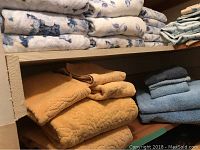 Shelving with stacks of folded bath towels in blue, yellow-orange, and cream colors.
