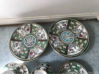 Two large dinner plates showing hand-painted Imari decorative patterns in green, white, red, blue, and gold with floral and geometric motifs