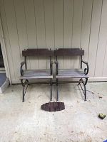 Two iron base porch bench chairs with wood seats and backs. One chair is missing a slat which is shown separately on the ground in front.