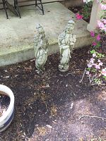 Two tall concrete statues of Asian-style women standing on soil near a concrete ledge, with visible wear and weathering.