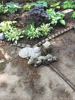 Photo of all three concrete yard sculptures: cat, dog, and dragon, placed on an outdoor pathway near garden plants.