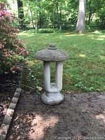 Mushroom-shaped concrete yard lantern placed on ground next to a flowering bush and lawn.