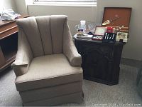 Vintage channel back arm chair in neutral beige fabric with visible channel back design and hardwood frame next to vintage dark hardwood side table.