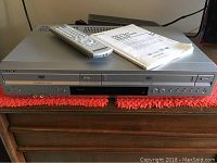 Full frontal view of Sony DVD VCR combo player on wooden dresser with red cloth underneath, remote and manual placed on top of unit.
