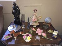 Full view of assorted decorative items on a wooden table, showing ceramic and metal figurines, floral pieces, coins, and miscellaneous collectibles.