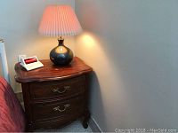 Bedside table with table lamp and digital alarm clock on top in corner of room