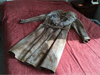 Full front view of vintage suede coat with fur collar and belt, laid on red surface