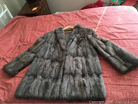 Front view of a full-length brown fur coat laid flat on a surface showing long sleeves and structured collar.