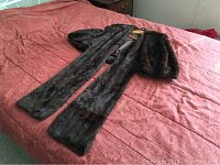 Full view of vintage fur cape laid out on bed showing length, sleeves, and collar.