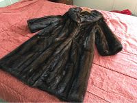 Full view of vintage ladies fur coat laid out flat on bed, showing the full length and fur texture.
