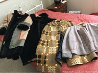 All four assorted ladies coats laid out on bed showing gray faux suede jacket, multi-color cape coat, black faux fur coat, and multi color faux fur-lined coat.