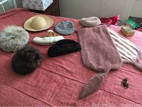 Photo of all assorted vintage men's and ladies' fur hats along with a fur shawl and two fur pins displayed on a red fabric surface.