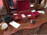 Overall view of vanity setup including sterling mirror, jewel box open with jewelry, travel books, and small clock on wooden dresser.