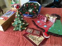Assorted Christmas decorations including ceramic light-up tree, ornaments, wreath, table decorations, and tissue wrapping paper arranged on a surface.