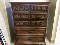 Front view of vintage chest of drawers showing all drawers and decorative carved panels on the upper drawers.