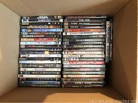 Top down view of DVDs in cardboard box showing assorted movie titles stacked horizontally and vertically.