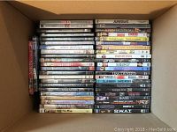 Photo showing a selection of approx. 45 DVDs stacked vertically in a cardboard box, titles visible include Don Jon, Silver Linings Playbook, American Hustle, Gran Torino, Minor Mishaps, and others.