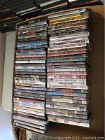 Stack of DVD cases showing a variety of movie and TV show titles, mostly in jewel case packaging, assorted genres visible.