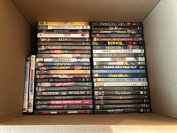 Overhead view of a box filled with DVDs stacked vertically showing titles from Kings of Comedy to Anne B. Real