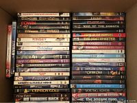 Photo showing a variety of DVD cases stacked side by side in a box, many titles visible, from 'Taken L'Enlèvement' to 'Young Adam' and 'The Answer'.