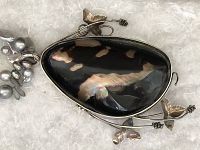 Close-up of large opium-shaped pearl pendant with sterling silver floral and leaf settings, showing dark iridescent colors and detailed metalwork.