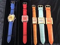 Five Joan Rivers watches laid out in black presentation trays, showing variety of band colors and watch face shapes.