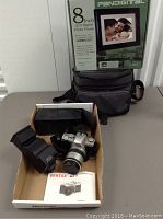 The full lot shown on table with Pandigital photo frame box behind and Pentax camera with lens and camera manual in a box