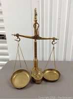 Full view of vintage brass balance scale with two hanging pans, central ornate column, and balance beam with hooks for pans.