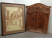 Framed artwork with sepia drawing of colonial balconies next to carved wooden mirror