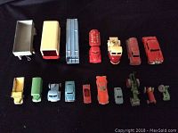 Top-down view of full assortment of 17 diecast toy vehicles including various trucks, cars, and tractors arranged in two rows on a black background.