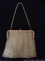 Full view of purse against black background showing overall shape, frame, clasp and chain handle.