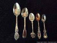Five vintage sterling silver spoons with varied ornate designs arranged on black background.