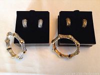 Two sets of Joan Rivers earrings and bracelets displayed side by side on black pads showing the textured pattern and color differences.