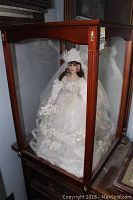 Full view of the porcelain bride doll in the glass and wooden display case showing the front and side profile.