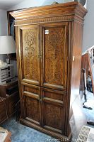 Front view of tall wooden armoire with carved floral designs on upper door panels and drawers below.