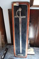 Full view of commemorative sword in wooden display case with black fabric backing.